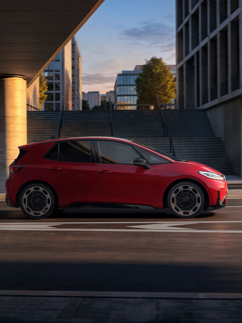 [AI-modified] – Seitenansicht eines roten VW ID.3 GTI während der Fahrt unter einer Brücke in der Stadt.