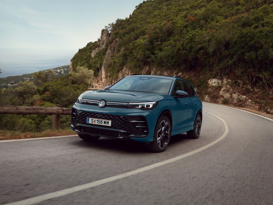  Ein blauer VW Tiguan R-Line eHybrid fährt auf einer kurvigen Landstraße.