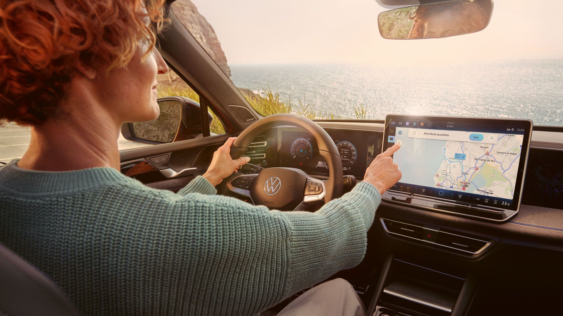 Frau sitzt auf dem Fahrersitz eines geparkten VW Tiguan und bedient den Touchscreen des Infotainment-Systems mit Kartenansicht.