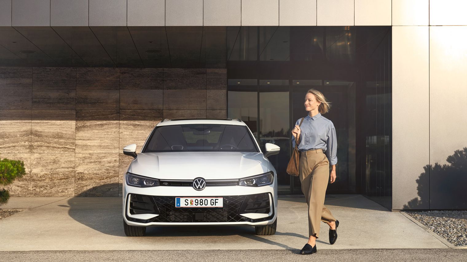 Frontansicht eines weißen VW Passat R-Line, eine Frau geht an ihm vorbei.