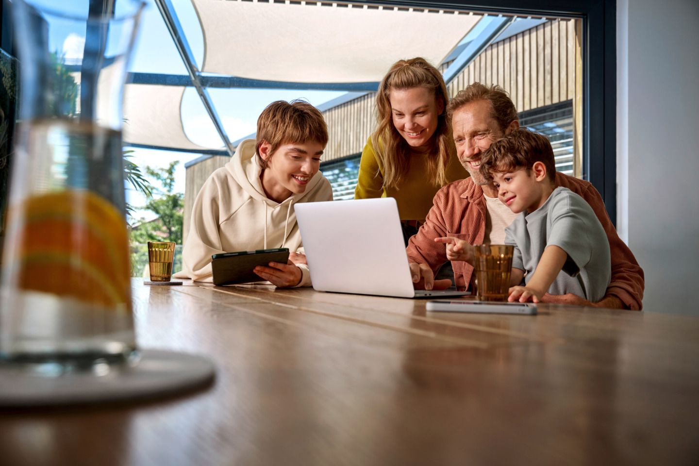 Eine Familie ist um einen Tisch versammelt und schaut fröhlich auf einen Laptop-Bildschirm