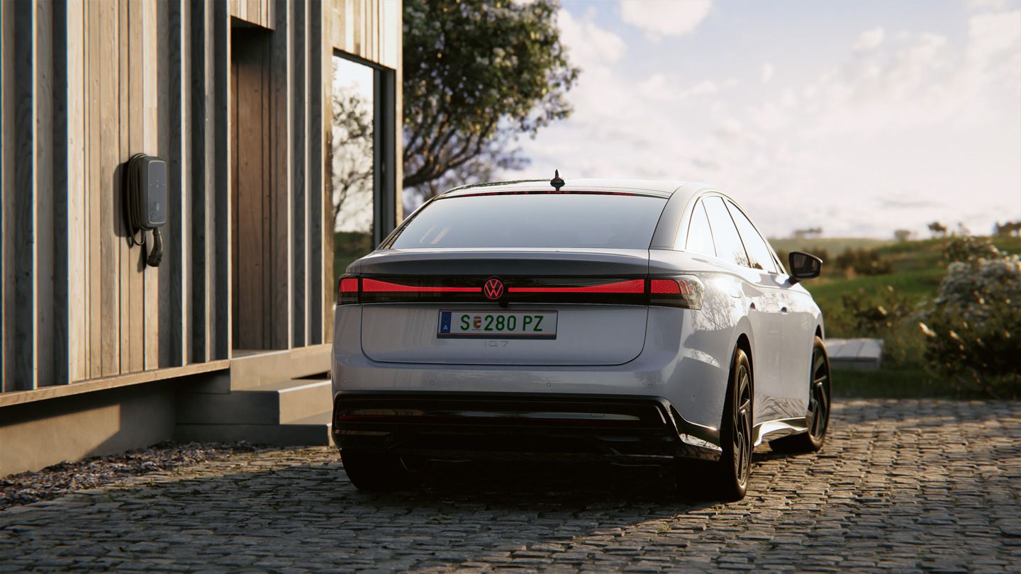 Heckansicht eines VW ID.7, der neben einer Ladesäule steht. Die Heck-Lichtsignatur mit Volkswagen-Logo leuchtet rot.