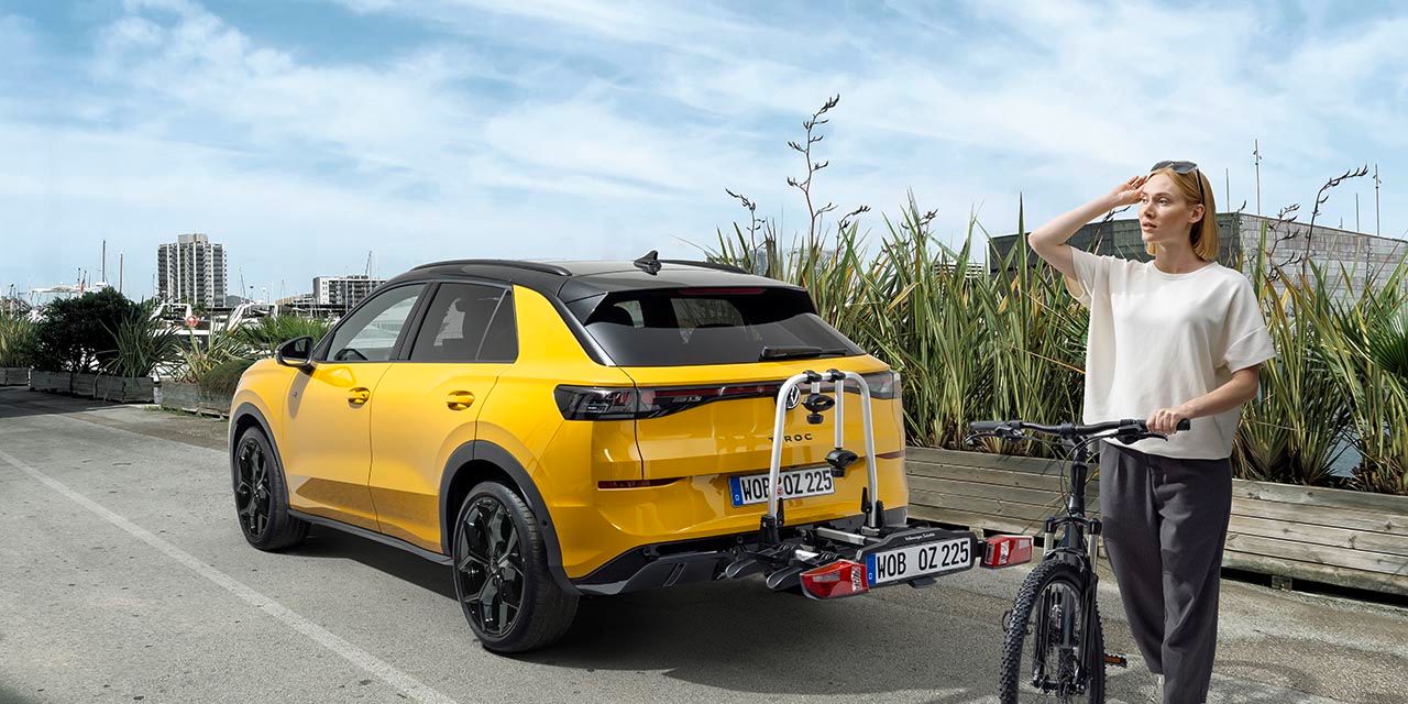 Eine Person mit einem Fahrrad steht neben einem gelben Volkswagen T-Roc mit Fahrradheckträger.