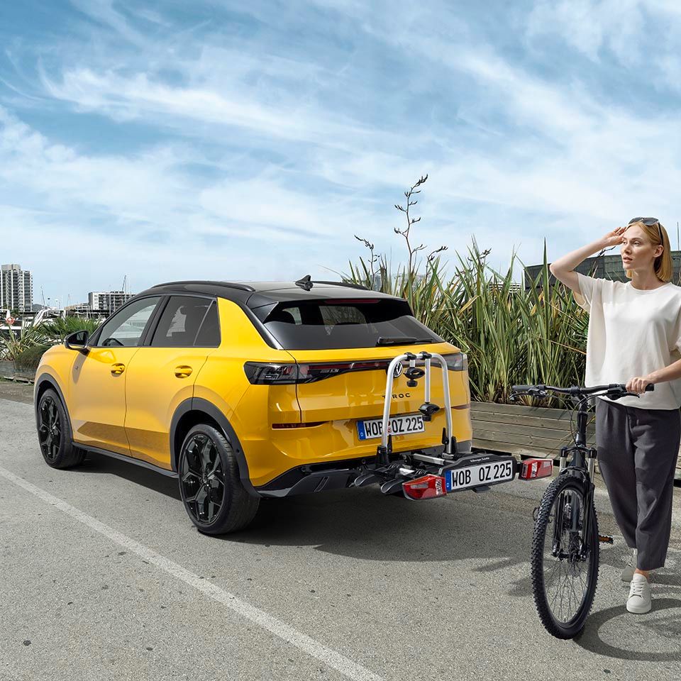 Eine Person mit einem Fahrrad steht neben einem gelben Volkswagen T-Roc mit Fahrradheckträger.
