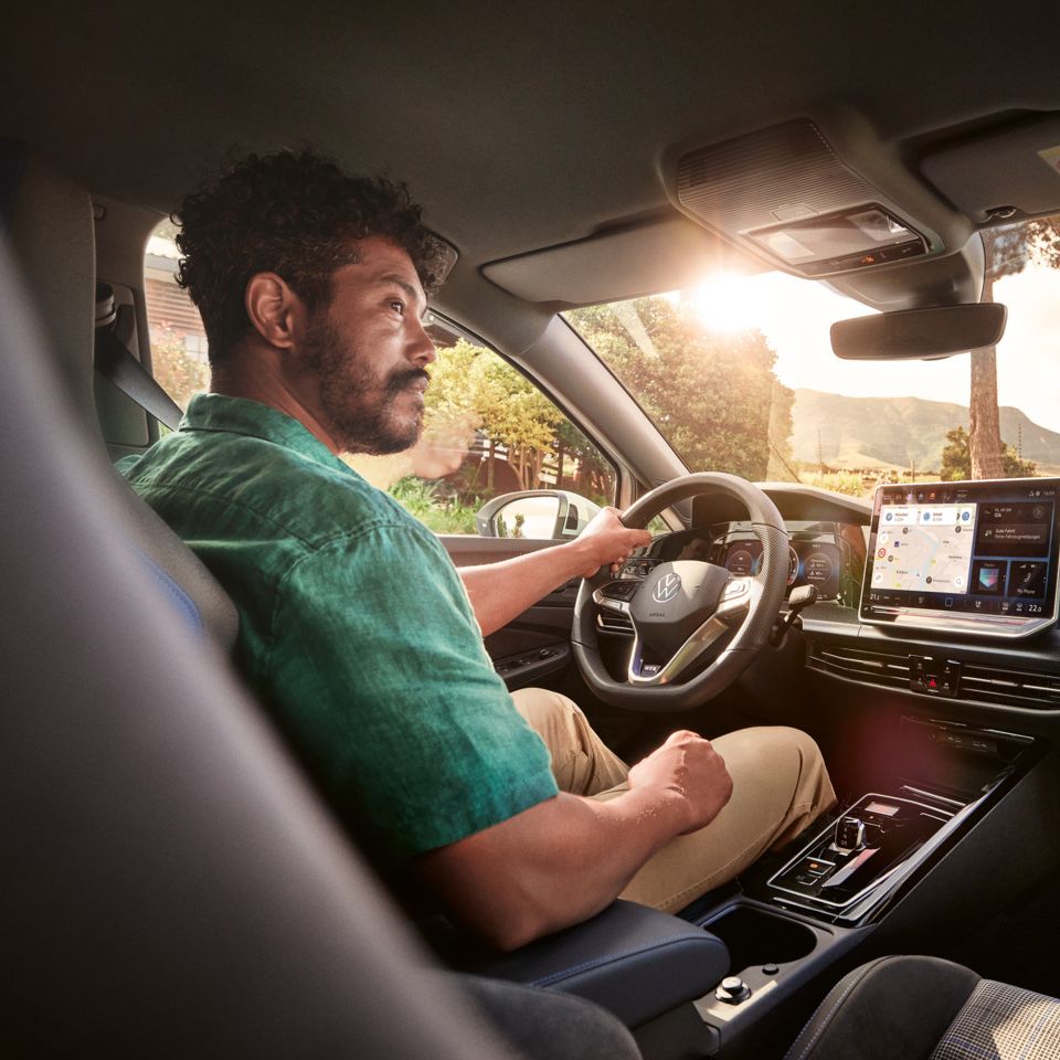 Person am Fahrersitz mit Hand am Lenkrad blickt in die rechte Richtung.