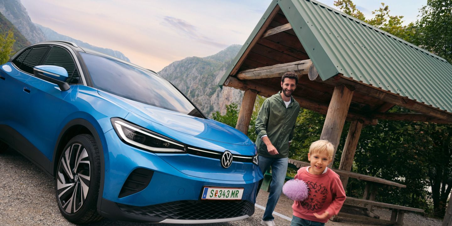 Vater und Sohn spielen mit einem Ball, daneben steht ein blauer VW ID.4.