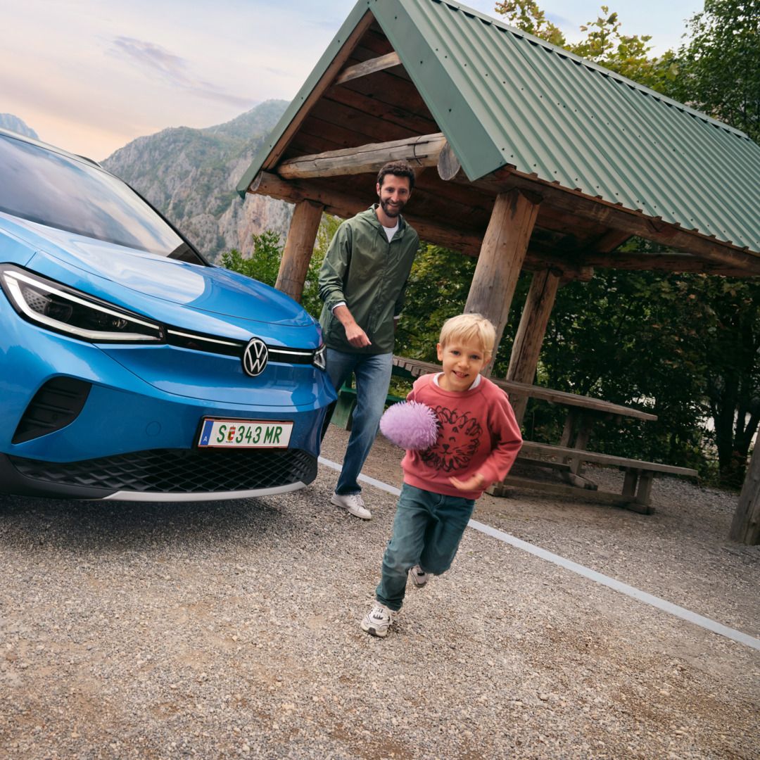 Vater und Sohn spielen mit einem Ball, daneben steht ein blauer VW ID.4.