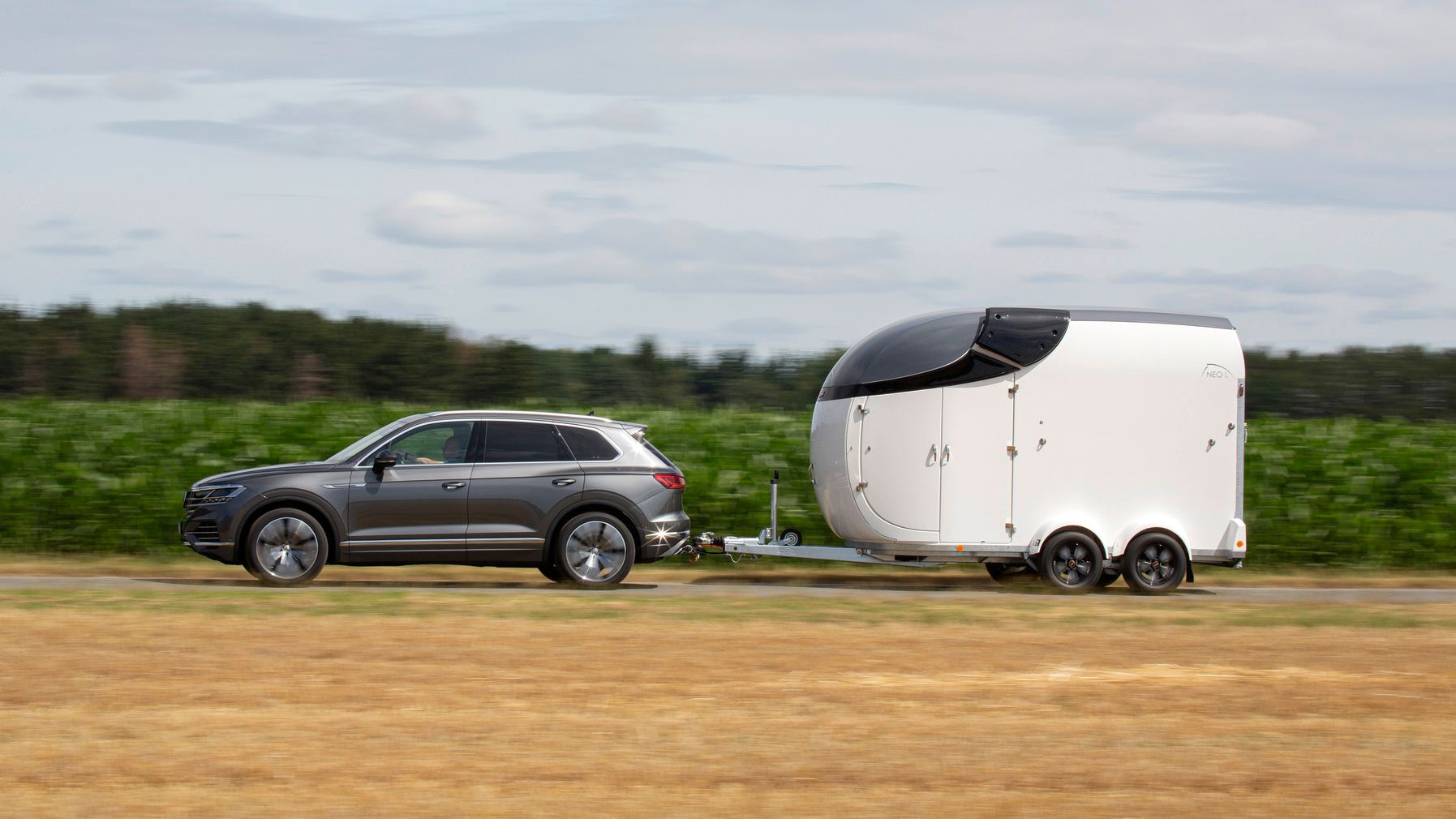 Ein dunkelgrauer VW Touareg zieht einen großen Transportanhänger.