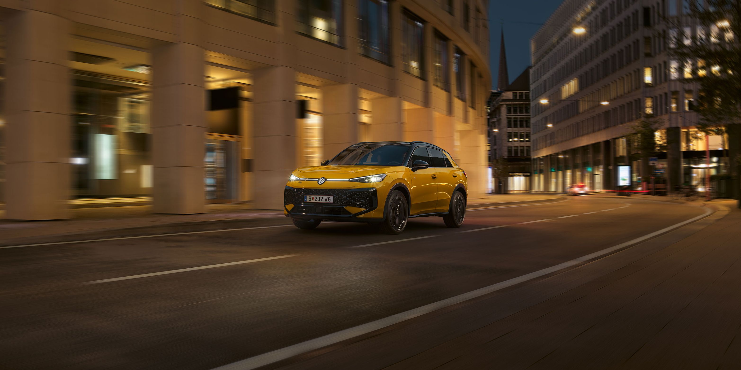 Ein gelber VW T-Roc R-Line fährt nachts durch eine urbane Umgebung.