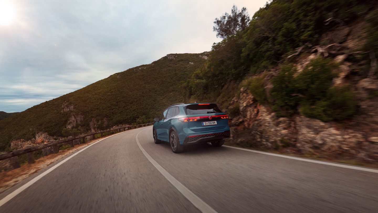 Roter VW Tiguan in Heckansicht fährt durch eine bergige Landschaft.