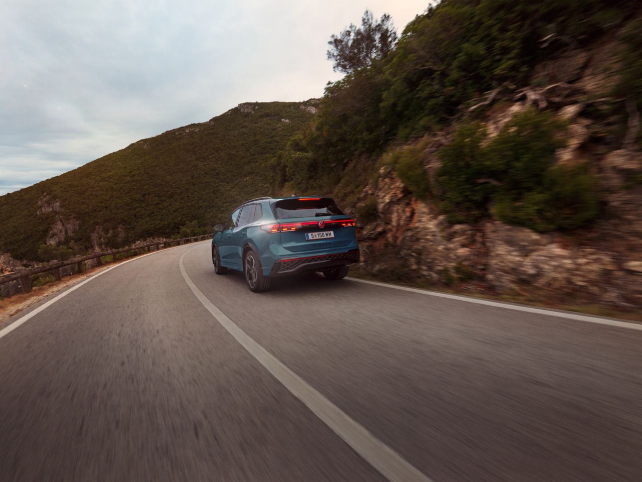 Roter VW Tiguan in Heckansicht fährt durch eine bergige Landschaft.