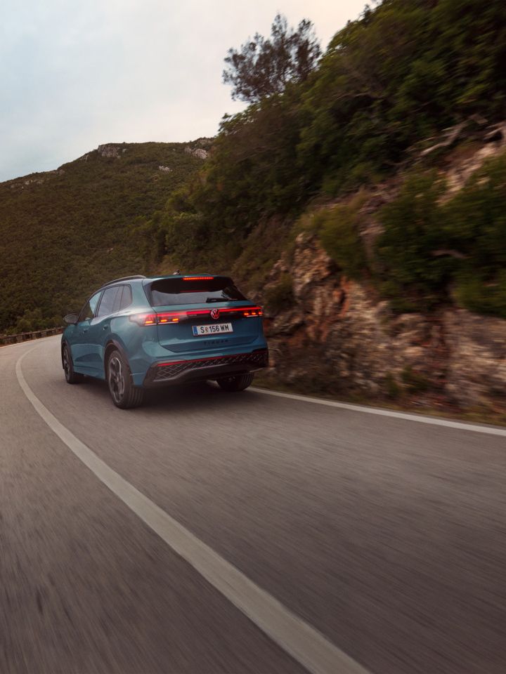 Roter VW Tiguan in Heckansicht fährt durch eine bergige Landschaft.