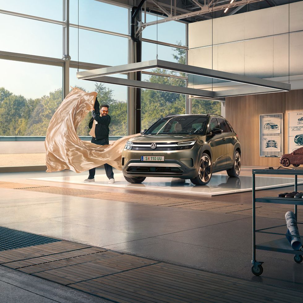 Ein Mann zieht ein großes Tuch von einem grünen VW ID. Cross, der in einem minimalistisch eingerichteten Designstudio steht.