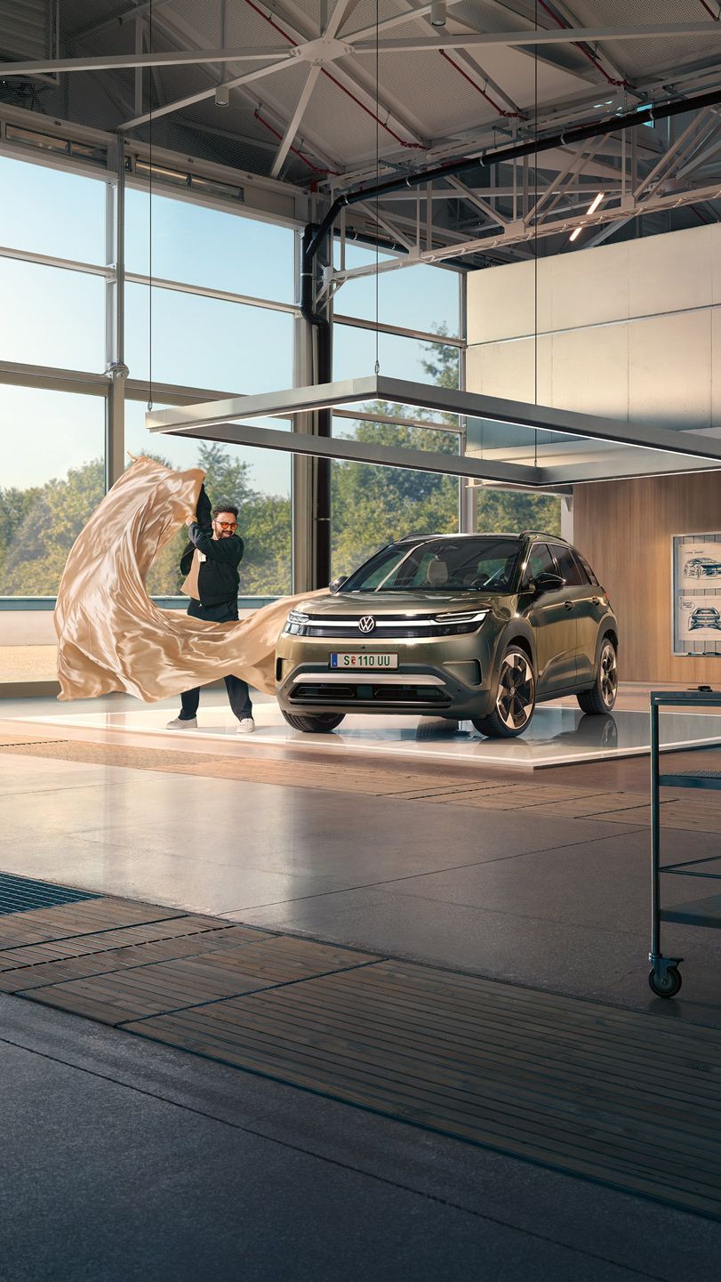 Ein Mann zieht ein großes Tuch von einem grünen VW ID. Cross, der in einem minimalistisch eingerichteten Designstudio steht.