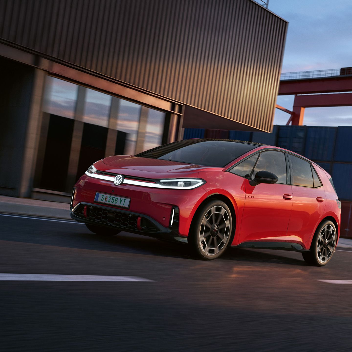 [AI-modified] – Ein roter VW ID.3 GTI fährt mit eingeschalteten Scheinwerfern und beleuchtetem Logo an einem Hafengebäude vorbei.