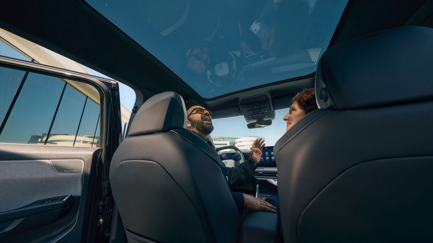 Ein Mann sitzt lachend auf dem Fahrersitz eines VW ID. Cross und schaut durch das geöffnete Panoramadach, eine Frau sitzt auf dem Beifahrersitz.