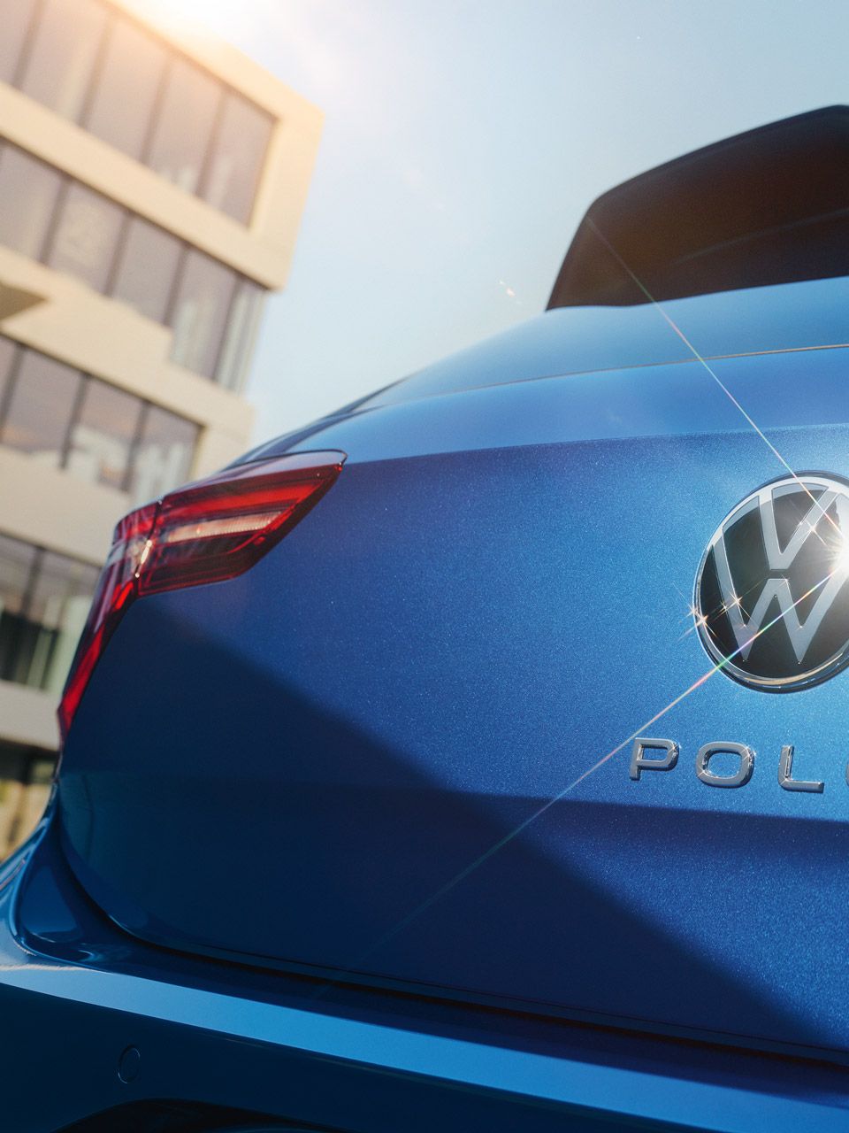 Die geschlossene Kofferraumklappe eines blauen VW Polo mit VW-Logo, in dem sich die Sonne spiegelt.