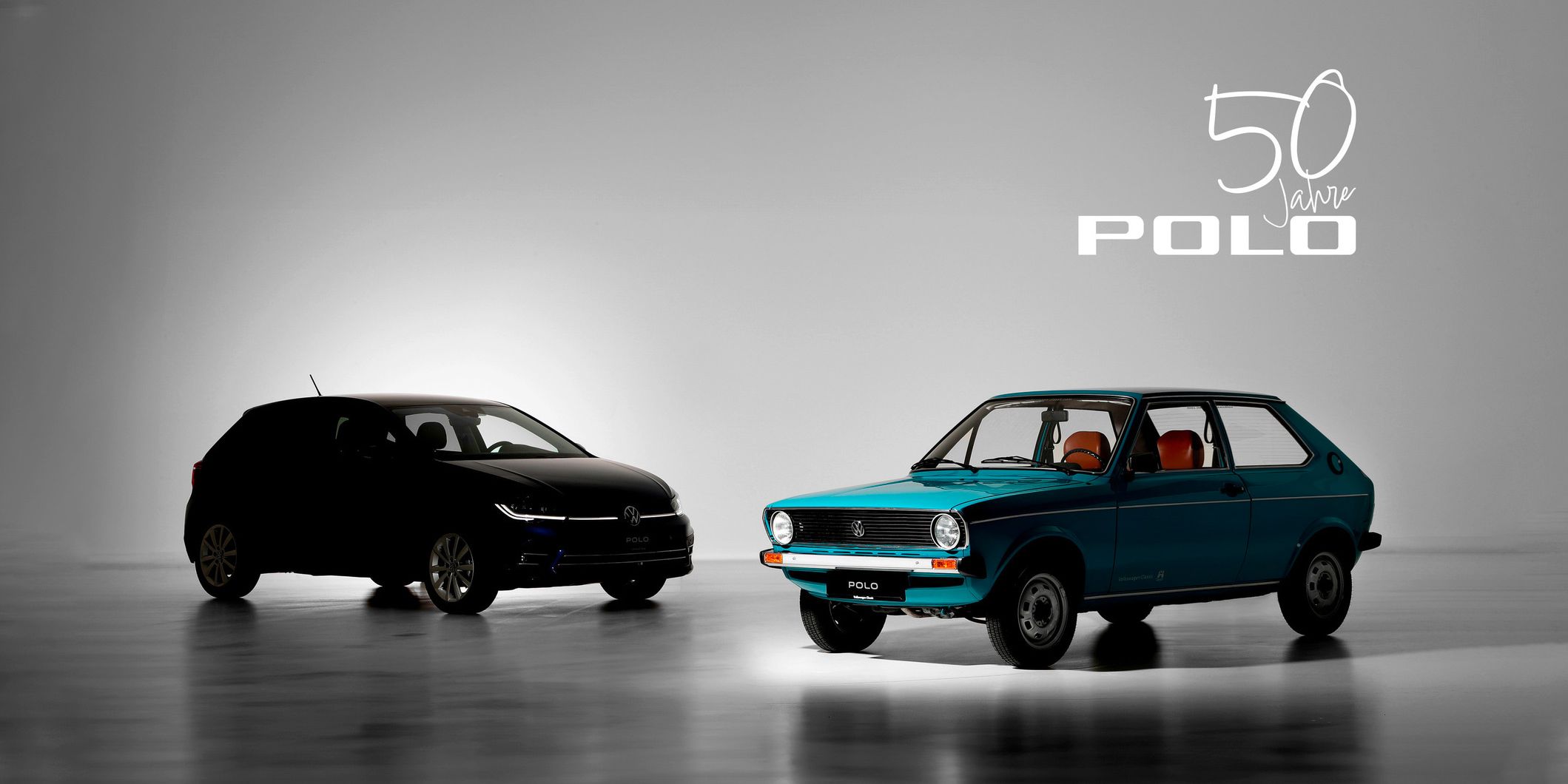 Zwei Volkswagen Polo Modelle nebeneinander: ein moderner schwarzer Polo und ein klassischer blauer Polo aus den frühen Jahren. Im Hintergrund steht „50 Jahre Polo“ geschrieben. Beleuchtung betont die Unterschiede zwischen den beiden Fahrzeugen.