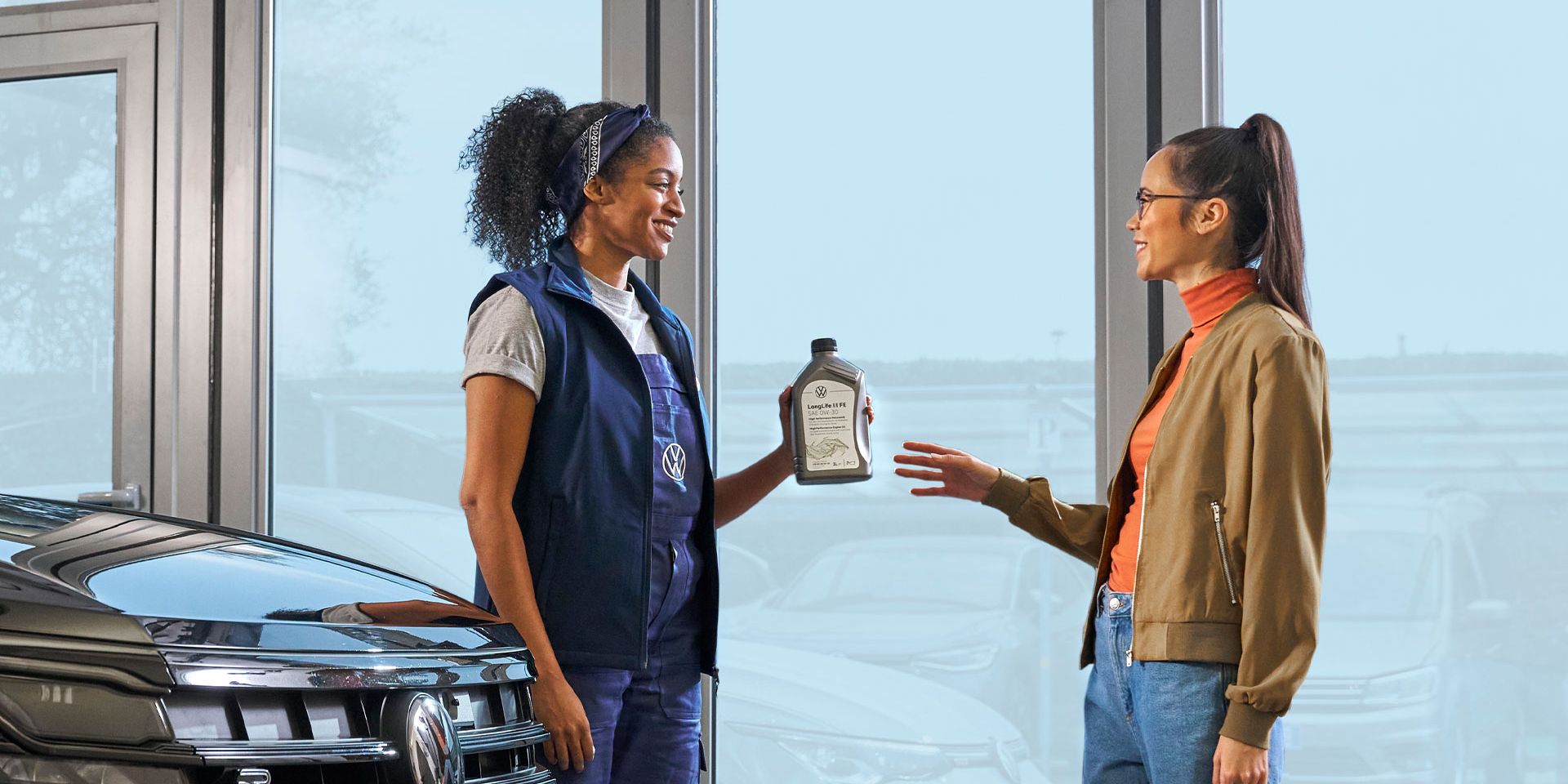 Eine Volkswagen Service Technikerin überreicht einer Kundin eine Ölflasche.