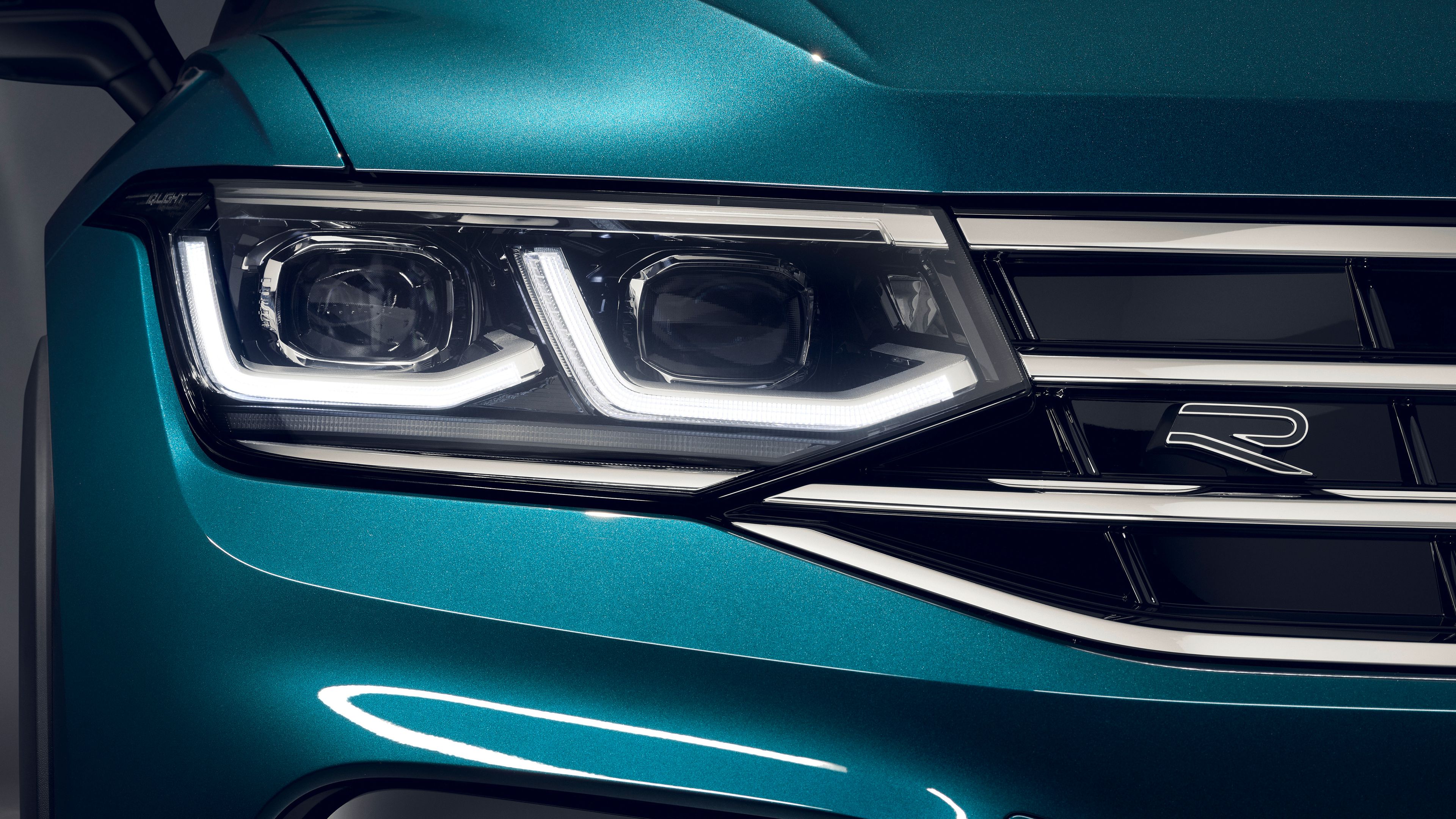 Nahaufnahme eines blauen Tiguan, das Scheinwerfer und einen Teil des Kühlergrills zeigt. Das Auto hat markante LED-Scheinwerfer und einen "R"-Emblem auf dem Grill. Das Bild betont die hochwertige und moderne Gestaltung des Fahrzeugs.