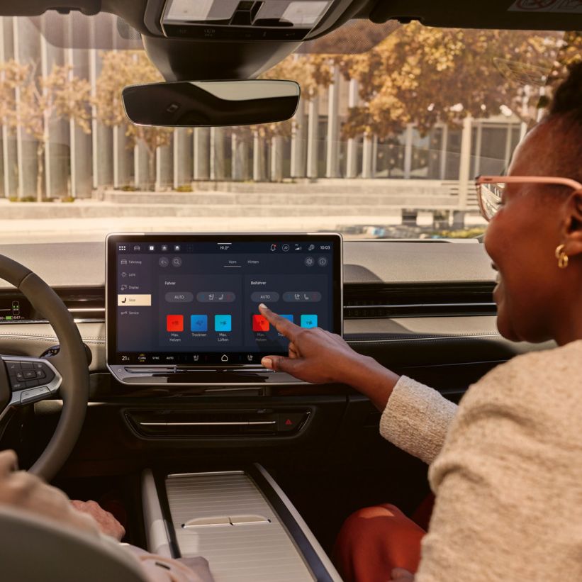 Zwei Frauen, die lachen, sitzen auf den Vordersitzen im VW ID.7 und bedienen das Infotainment-System.