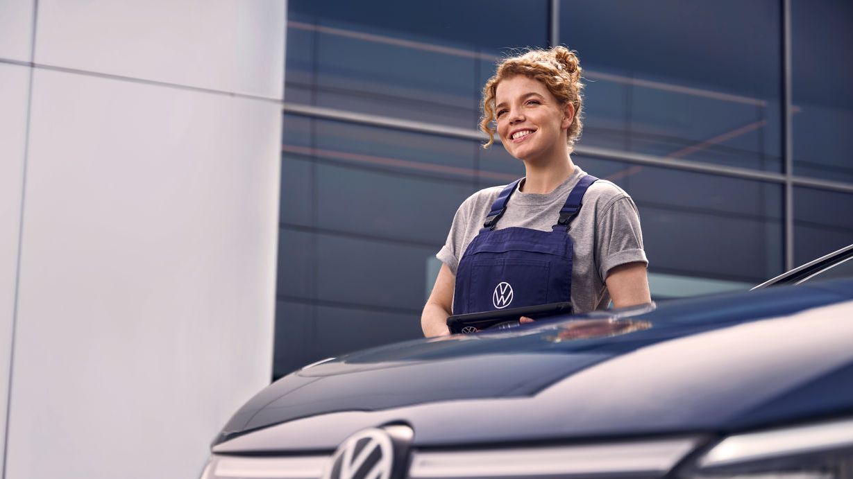 Eine Volkswagen Technikerin vor einer Volkswagen Werkstatt.