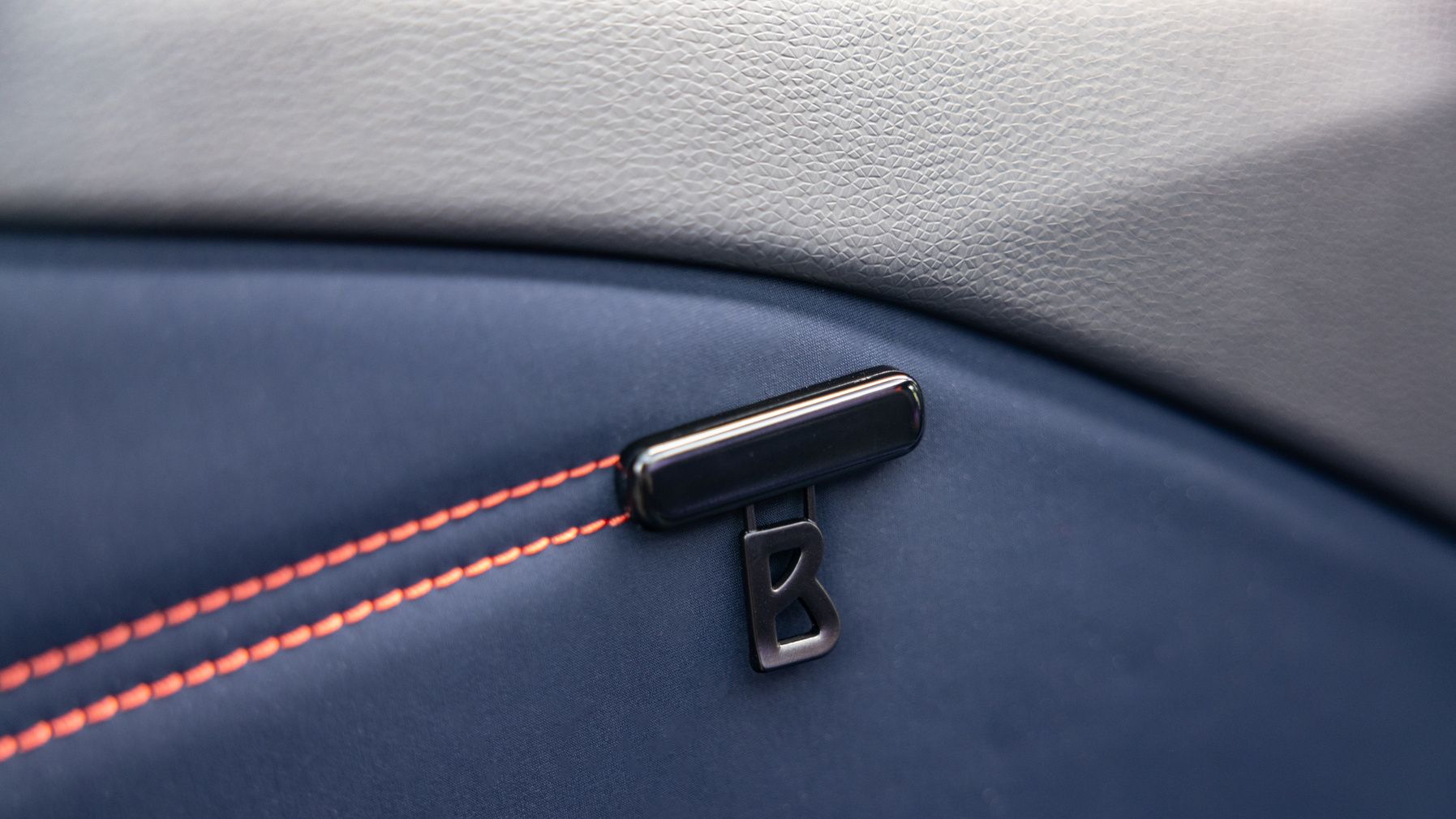 Detailaufnahme einer Autoinnenverkleidung mit blauer Polsterung und orangen Nähten. Ein schwarzes "B"-Emblem ist auf der Polsterung angebracht.