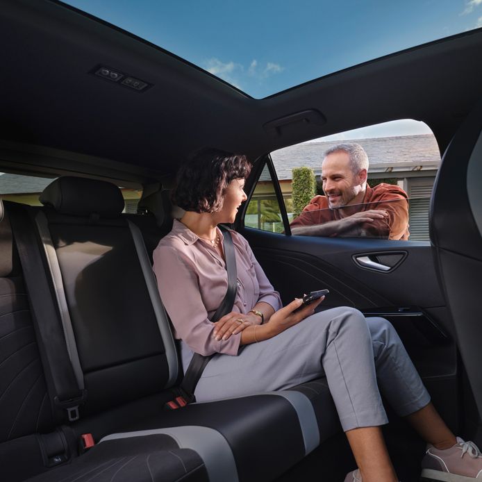 Eine Frau sitzt auf der Rückbank des VW ID.3 und redet mit einem Mann