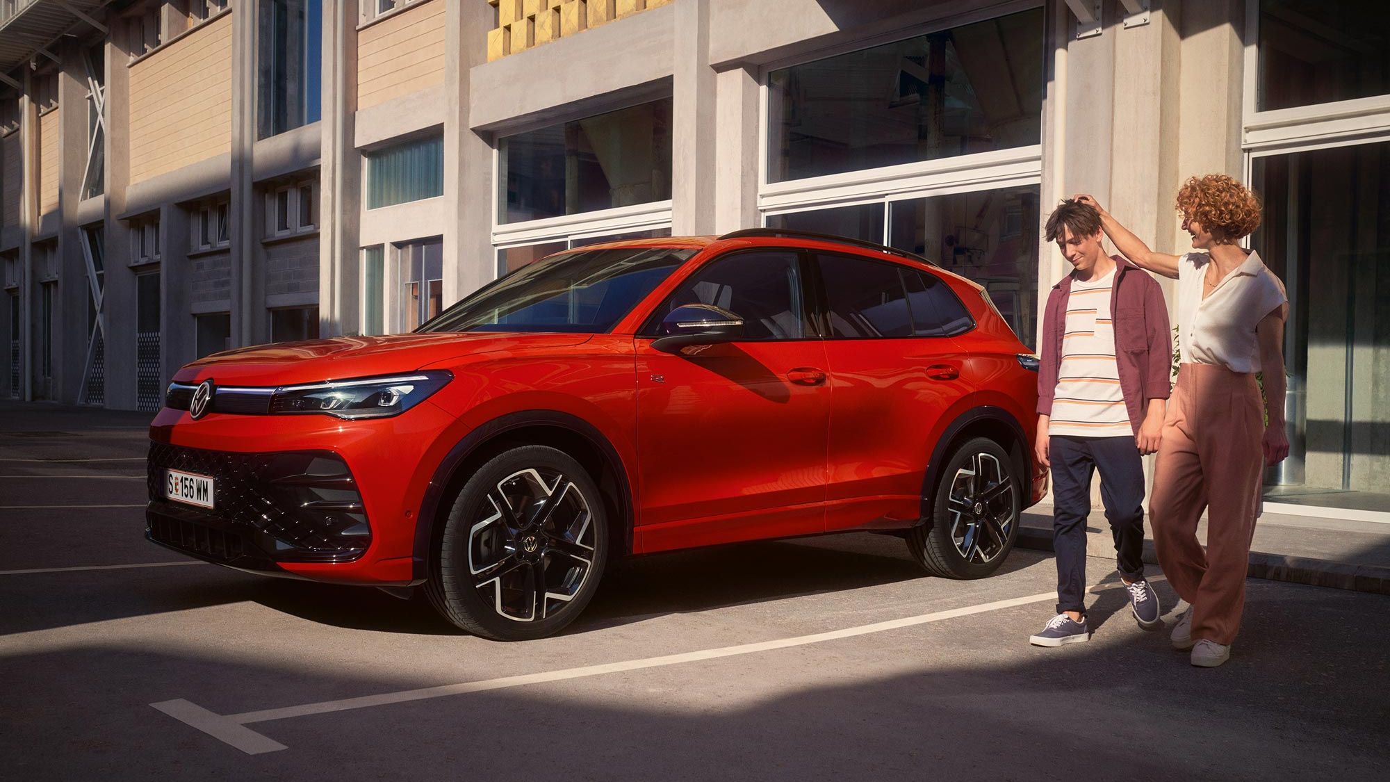 Mutter legt ihre Hand den Kopf ihres Sohnes, beiden gehen neben eines roten VW Tiguan R-Line her