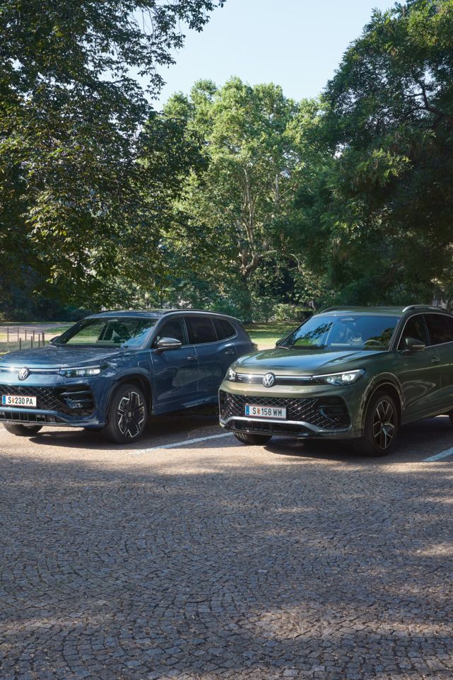 Blauer Tiguan R-Line Plug-In-Hybrid und grüner Tayron R-Line Plug-In- Hybrid parken nebeneinander im schattigen Parkbereich.